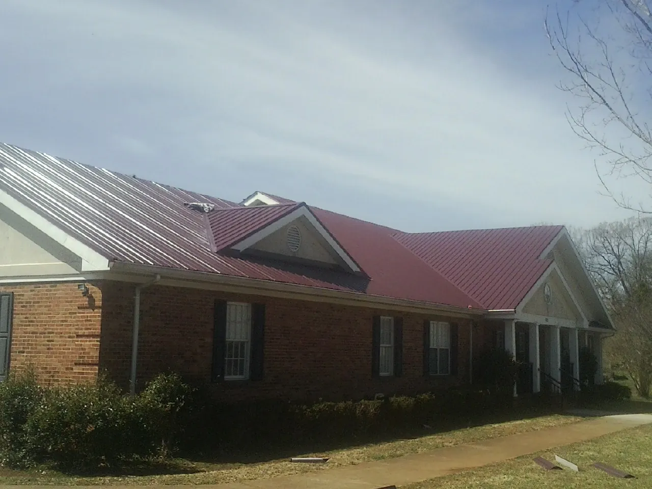 Red metal roof with gabled entries on a long brick building, from a Hail Damage Roof Repair job in Redwood City