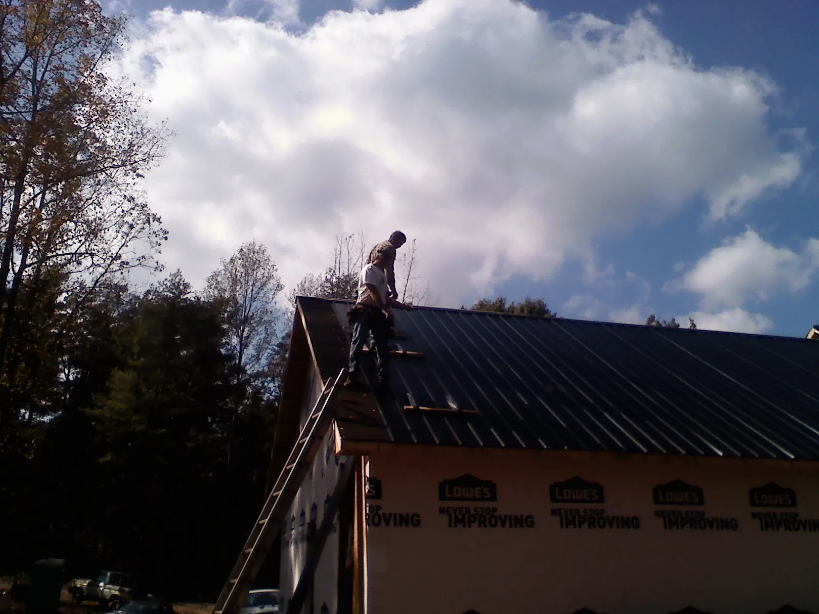 Roofer fastening dark metal panels high against a cloudy sky, from a Roof Inspection job in Redwood City