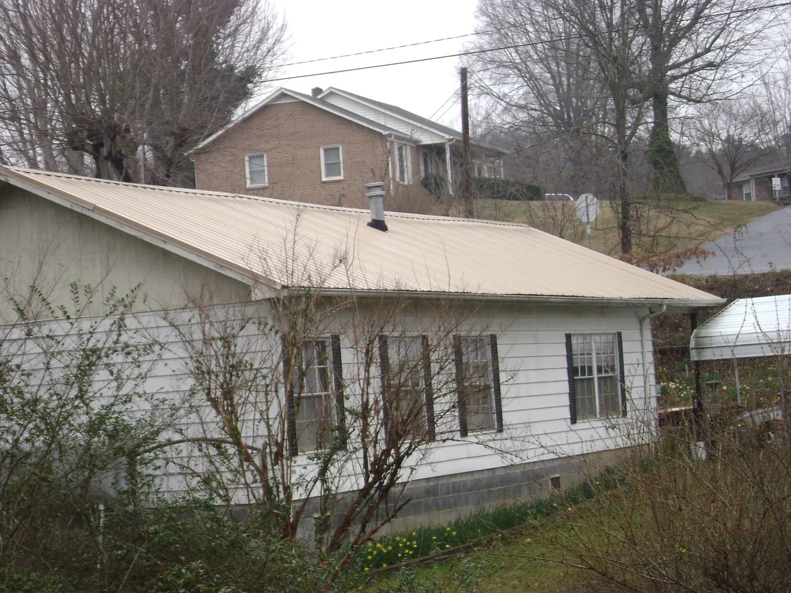 Tan metal roof on a white sided house set into a hillside — Commercial Roofing by Roofing Brothers in Redwood City